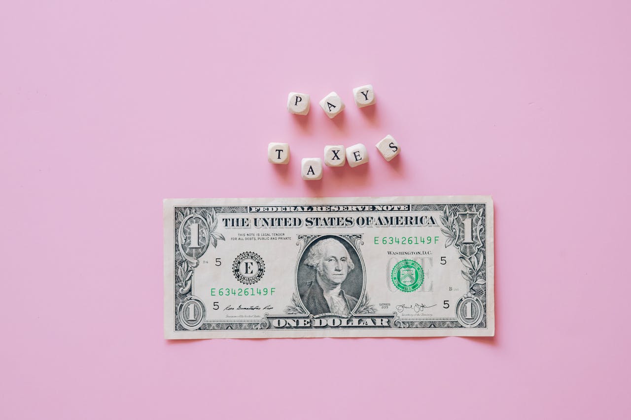 US one dollar bill on a pink background with pay taxes reminder cubes.